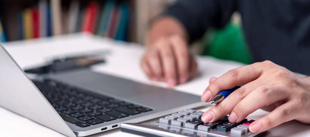 Large close-up of person using laptop & calculator.